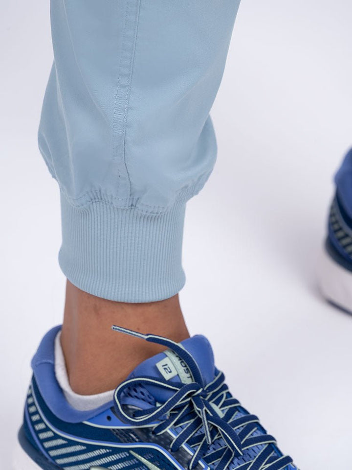 A young female LPN wearing an Epic by MedWorks Women's Yoga Jogger Scrub Pant in Blue Fog featuring elastic rib knit ankle cuffs.