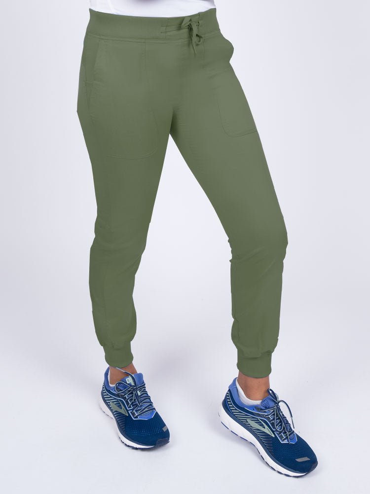 A female healthcare professional wearing the Epic by MedWorks Women's Yoga Jogger Scrub Pants in Olive size Large Tall featuring 2 slanted entry patch pockets on the front.