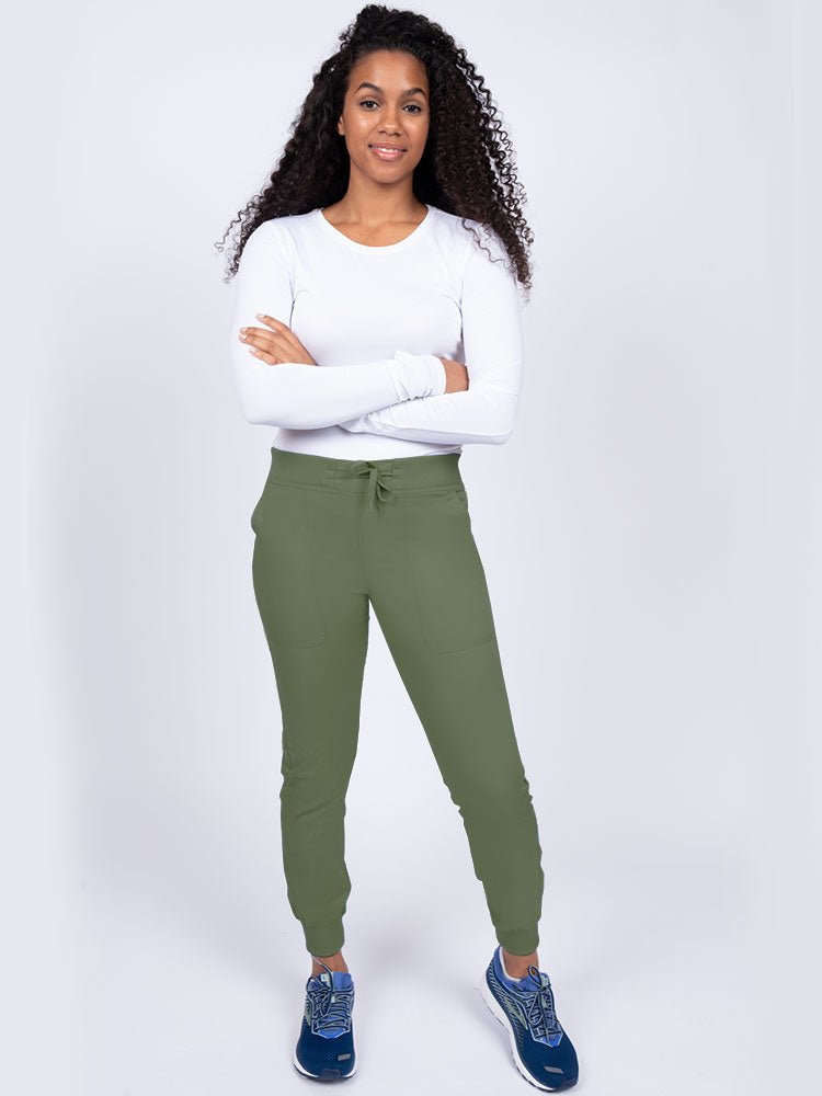 A young lady nurse wearing an Epic by MedWorks Women's Yoga Jogger Scrub Pant in Olive size Large Petite featuring stylish cover stitch detail throughout.