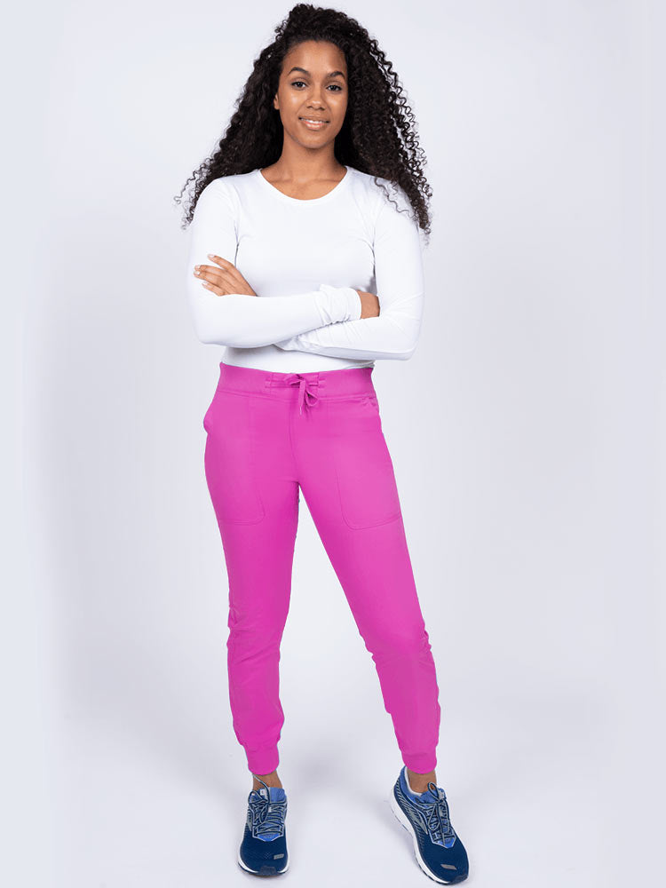 A young lady nurse wearing an Epic by MedWorks Women's Yoga Jogger Scrub Pant in Shocking Pink size Large Petite featuring stylish cover stitch detail throughout.