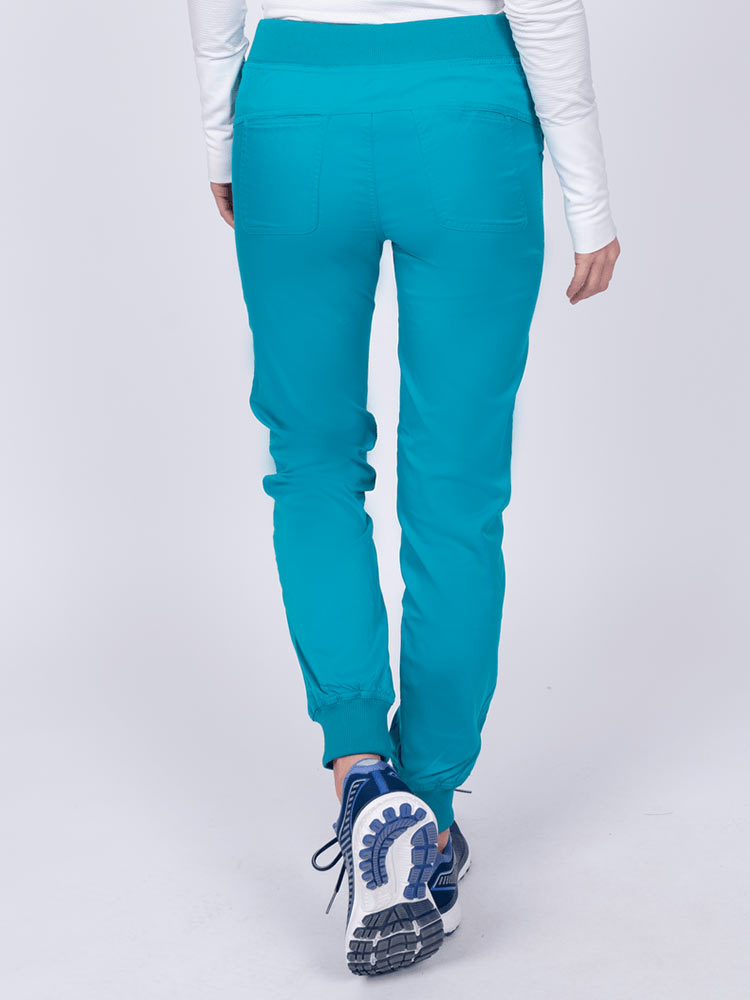 A young female Nurse Practitioner wearing an Epic by MedWorks Women's Yoga Jogger Scrub Pant in Teal size small featuring 2 back patch pockets.