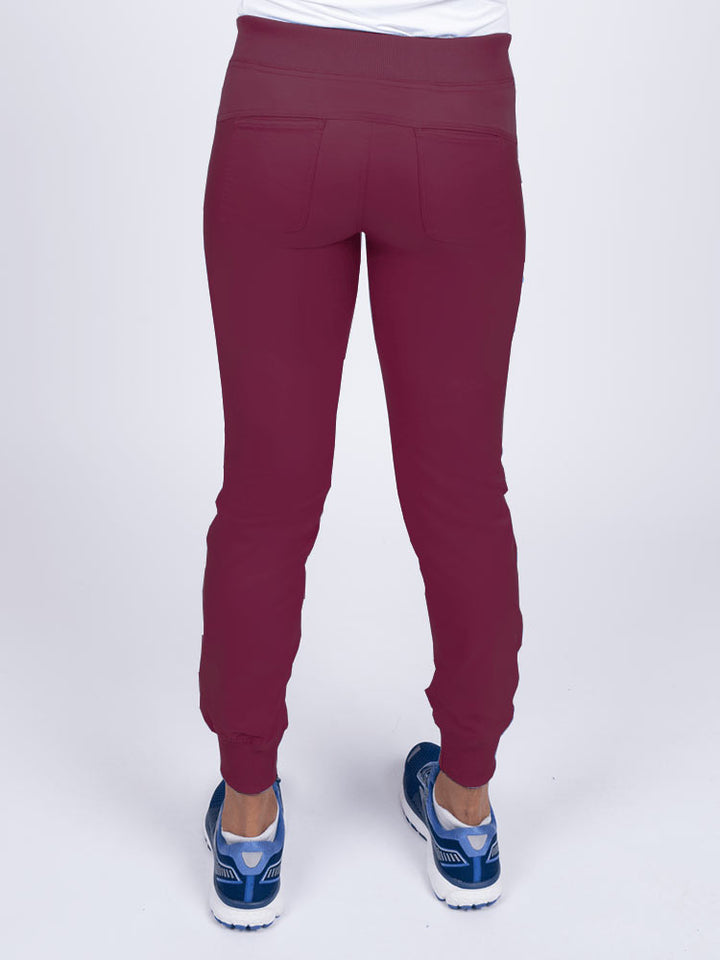 A young female Nurse Practitioner wearing an Epic by MedWorks Women's Yoga Jogger Scrub Pant in Wine  size small featuring 2 back patch pockets.