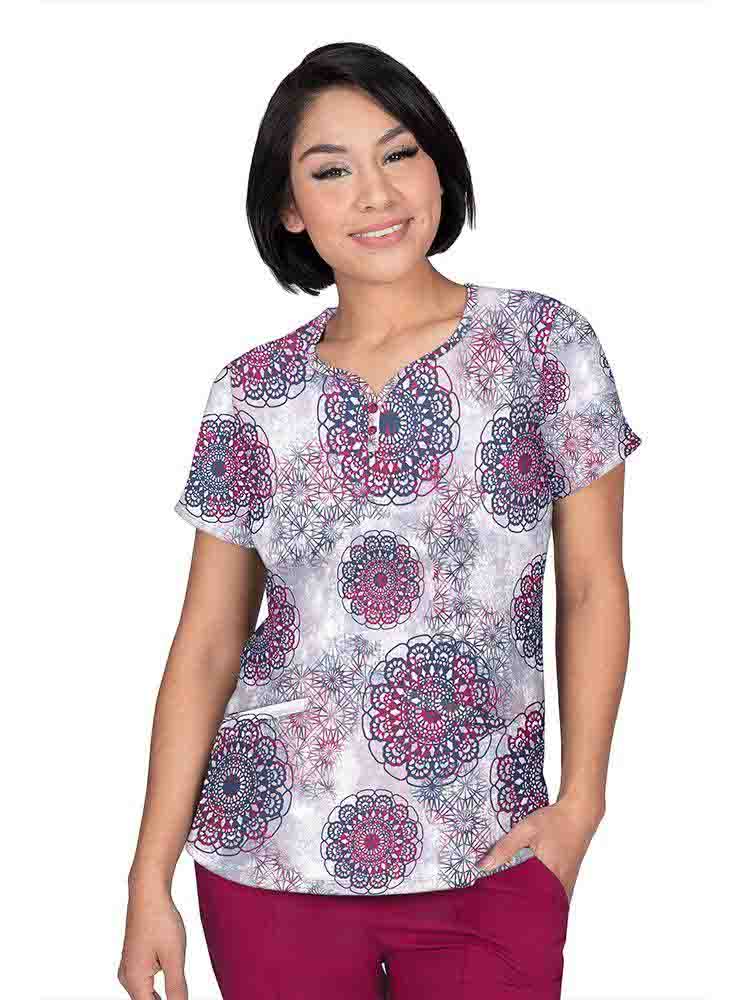 A young female Pediatric Nurse wearing a Premiere by Healing Hands Women's Isabel Scrub Top in "Dreamy Lace" featuring a y-neckline with decorative buttons.
