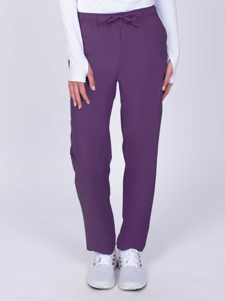 Young woman wearing a Luv Scrubs by MedWorks Women's Elastic Waist Cargo Pant in eggplant featuring one cargo pocket on the wearer's left side.