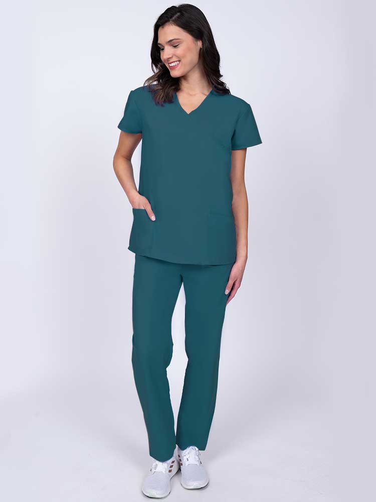 Young healthcare worker wearing a Luv Scrubs by MedWorks Women's Mock Wrap Scrub Top in Caribbean with 2 front patch pockets.