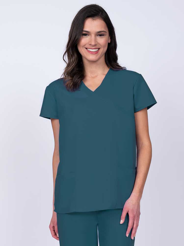 Young woman wearing a Luv Scrubs by MedWorks Women's Mock Wrap Scrub Top in Caribbean featuring a Y-neckline and side slits for additional range of motion.