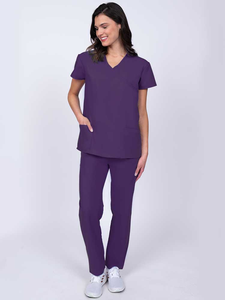 Young healthcare worker wearing a Luv Scrubs by MedWorks Women's Mock Wrap Scrub Top in eggplant with 2 front patch pockets.