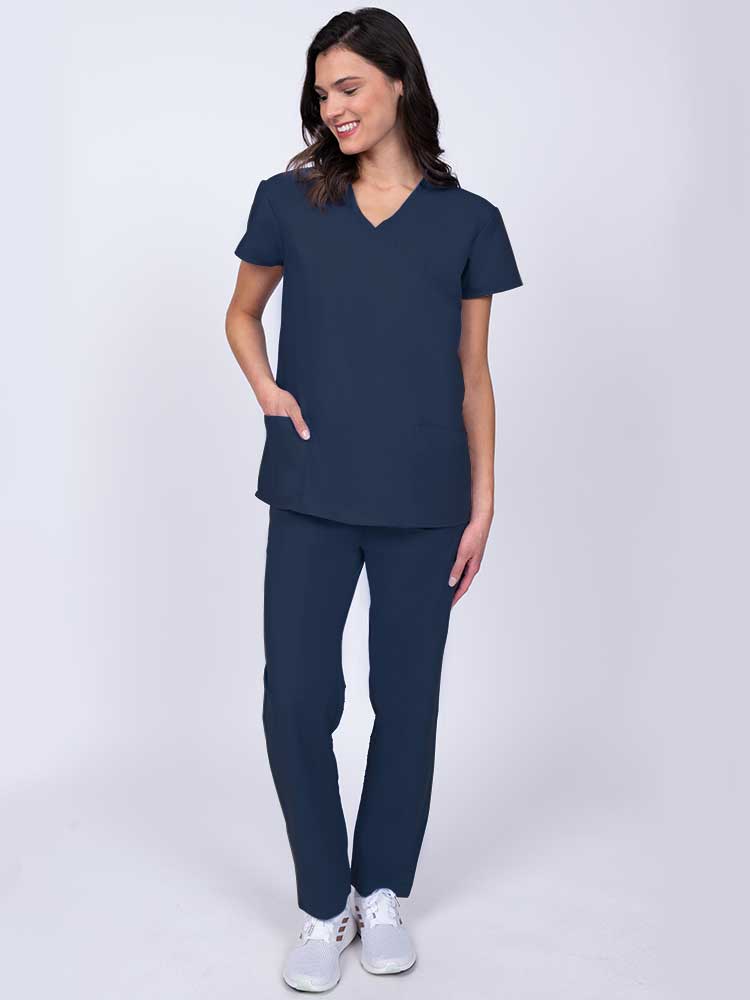 Young healthcare worker wearing a Luv Scrubs by MedWorks Women's Mock Wrap Scrub Top in navy with 2 front patch pockets.