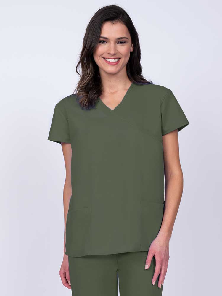 Young woman wearing a Luv Scrubs by MedWorks Women's Mock Wrap Scrub Top in olive featuring a Y-neckline and side slits for additional range of motion.
