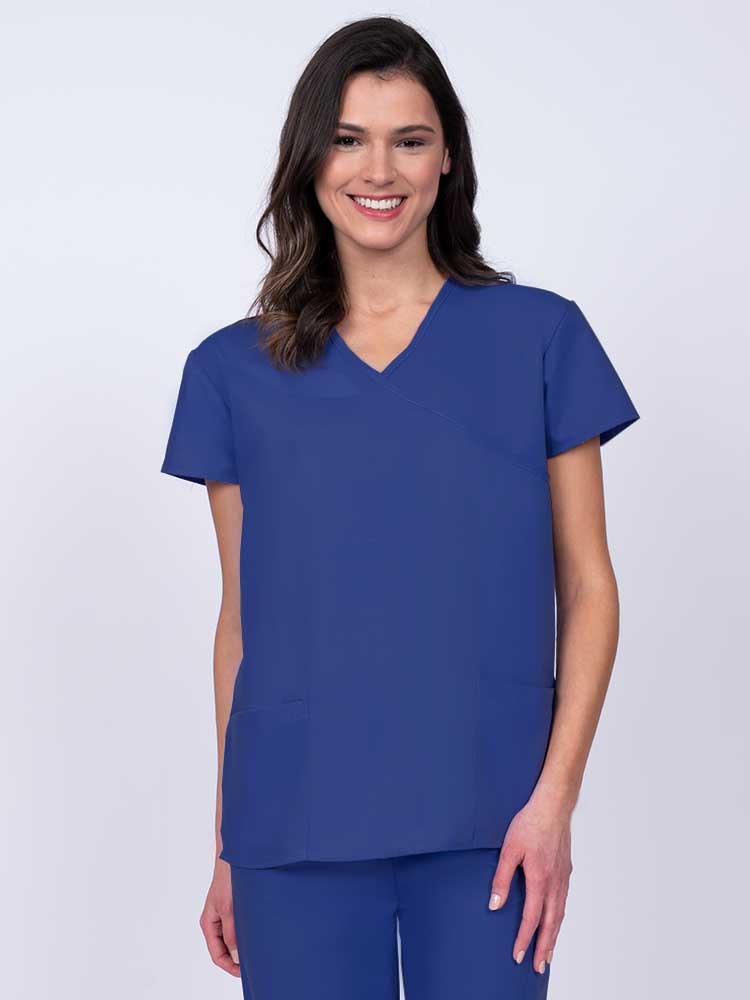 Young woman wearing a Luv Scrubs by MedWorks Women's Mock Wrap Scrub Top in royal featuring a Y-neckline and side slits for additional range of motion.