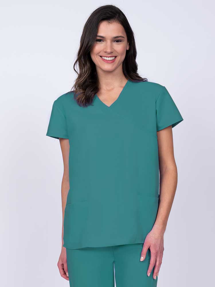 Young woman wearing a Luv Scrubs by MedWorks Women's Mock Wrap Scrub Top in teal featuring a Y-neckline and side slits for additional range of motion.