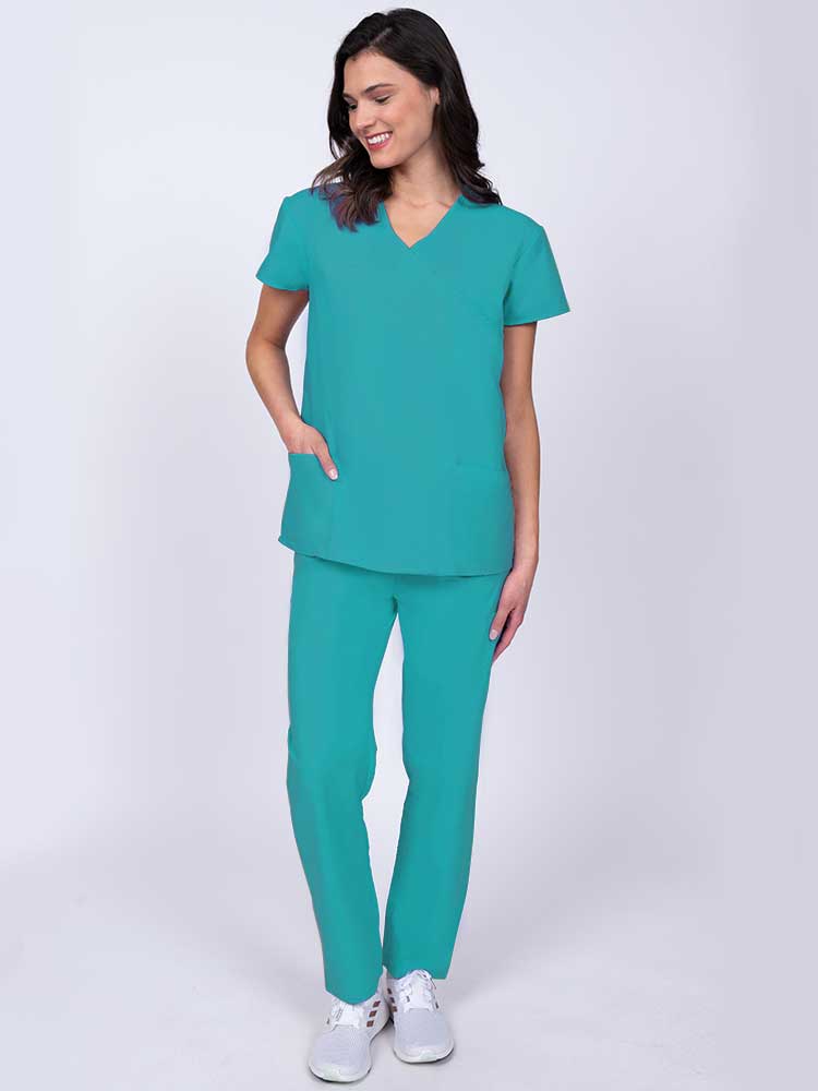 Young healthcare worker wearing a Luv Scrubs by MedWorks Women's Mock Wrap Scrub Top in turquoise with 2 front patch pockets.