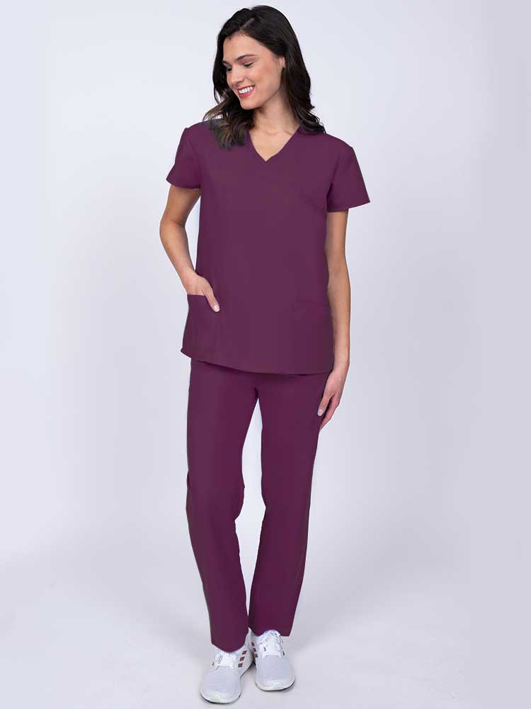 Young healthcare worker wearing a Luv Scrubs by MedWorks Women's Mock Wrap Scrub Top in wine with 2 front patch pockets.