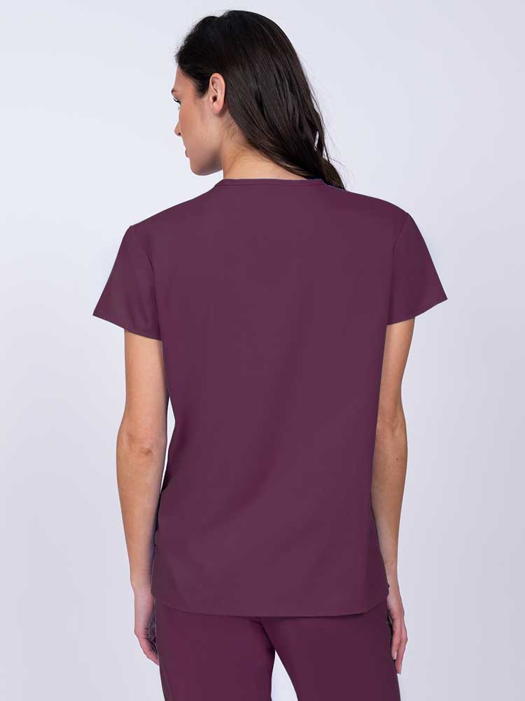 Woman wearing a Luv Scrubs by MedWorks Women's Pocketless Mock Wrap Scrub Top in wine with shoulder yokes to ensure a flattering fit.