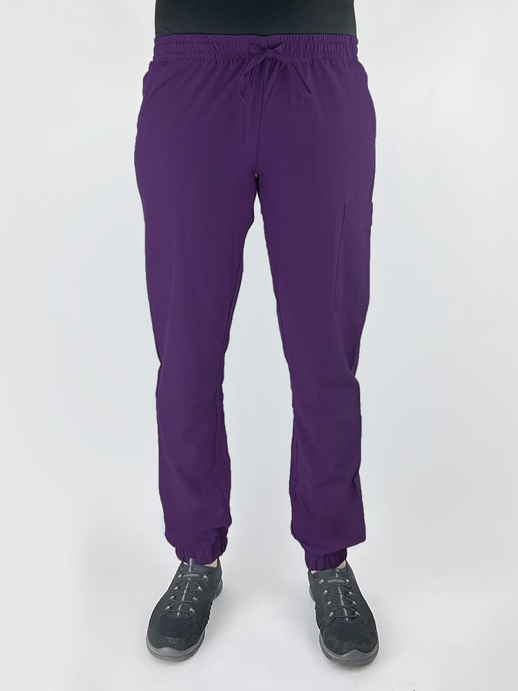Young female healthcare worker wearing a Luv Scrubs by MedWorks Women's Scrub Jogger in eggplant with 2 front slash pockets & 1 cargo pocket on wearer's left leg.