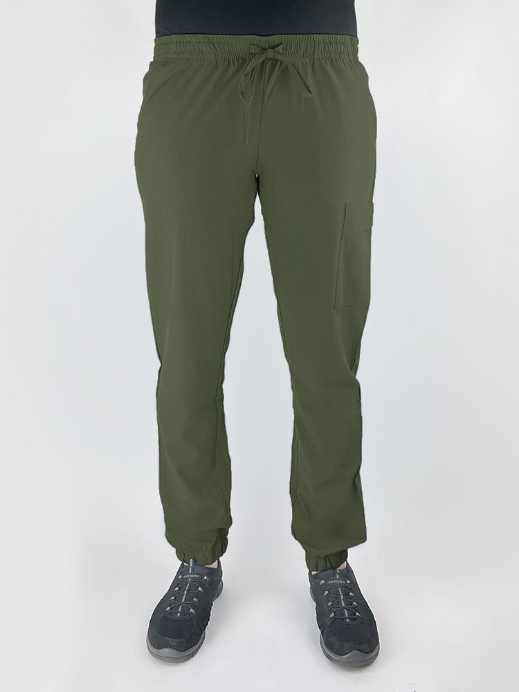 Young female healthcare worker wearing a Luv Scrubs by MedWorks Women's Scrub Jogger in olive with 2 front slash pockets & 1 cargo pocket on wearer's left leg.