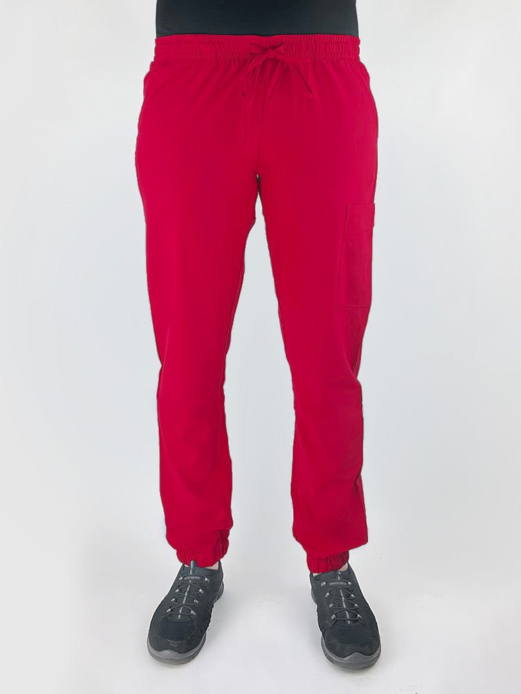 Young female healthcare worker wearing a Luv Scrubs by MedWorks Women's Scrub Jogger in red with 2 front slash pockets & 1 cargo pocket on wearer's left leg.