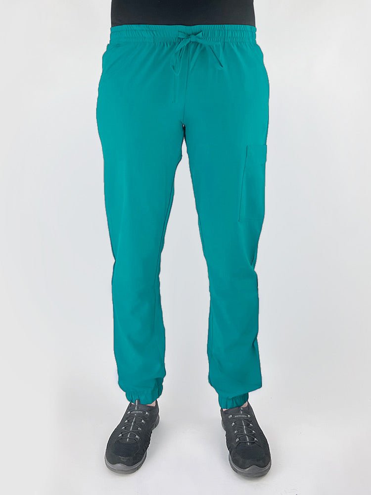 Young female healthcare worker wearing a Luv Scrubs by MedWorks Women's Scrub Jogger in teal with 2 front slash pockets & 1 cargo pocket on wearer's left leg.