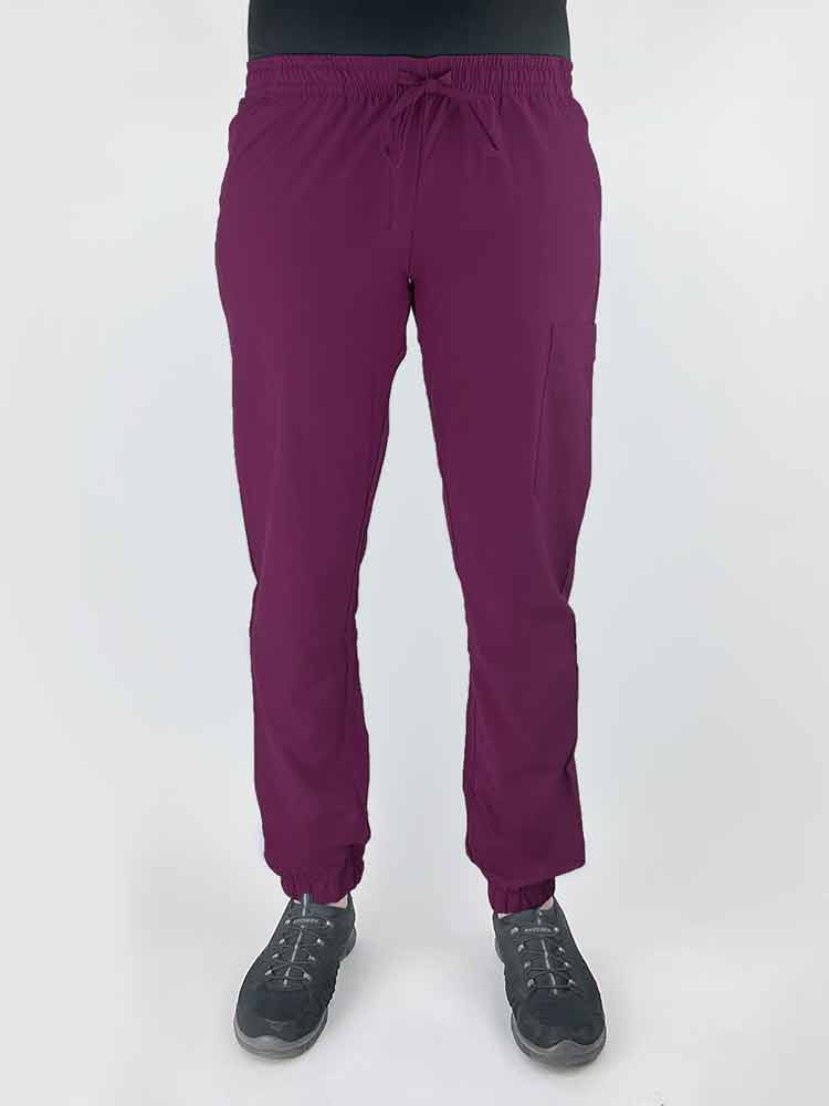Young female healthcare worker wearing a Luv Scrubs by MedWorks Women's Scrub Jogger in wine with 2 front slash pockets & 1 cargo pocket on wearer's left leg.