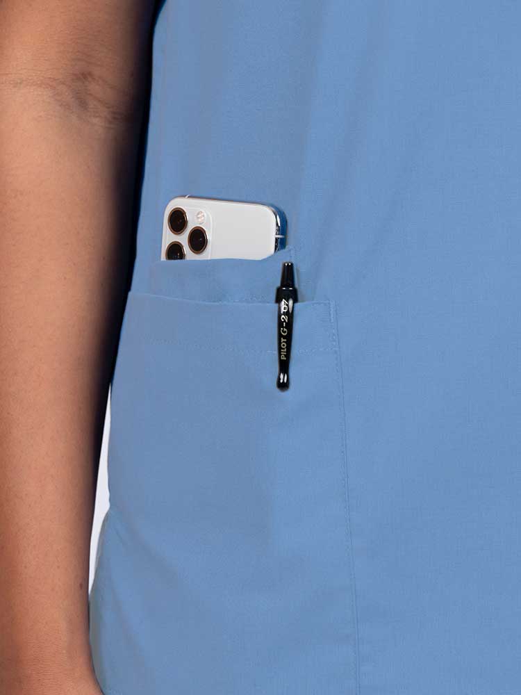 Young female healthcare worker wearing a Luv Scrubs by MedWorks Women's V-neck Scrub Top in ceil with a hidden utility pocket/pen slot on wearer's right side.