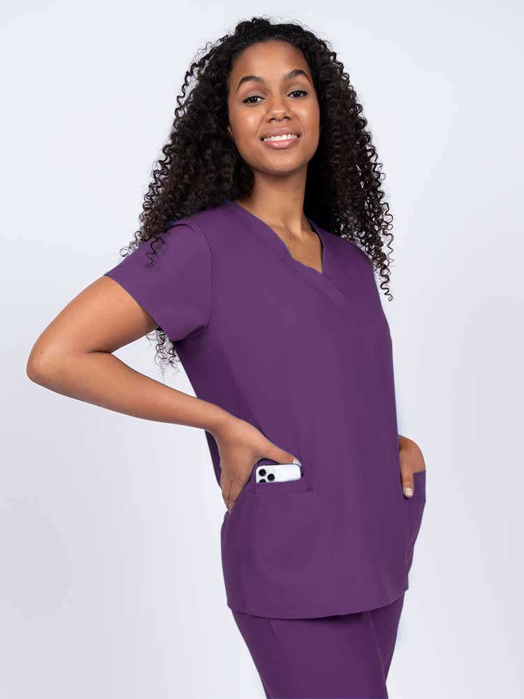 Young nurse wearing a Luv Scrubs by MedWorks Women's V-neck Scrub Top in eggplant with featuring short sleeves, and a total of 3 pockets.