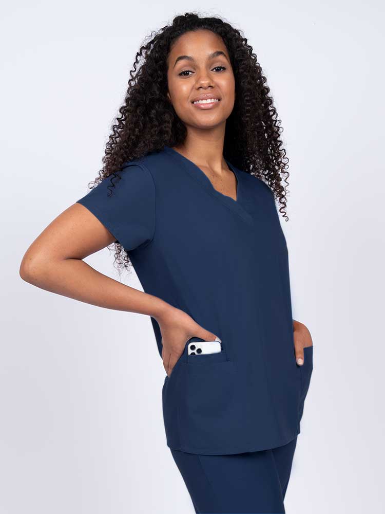 Young nurse wearing a Luv Scrubs by MedWorks Women's V-neck Scrub Top in navy with featuring short sleeves, and a total of 3 pockets.