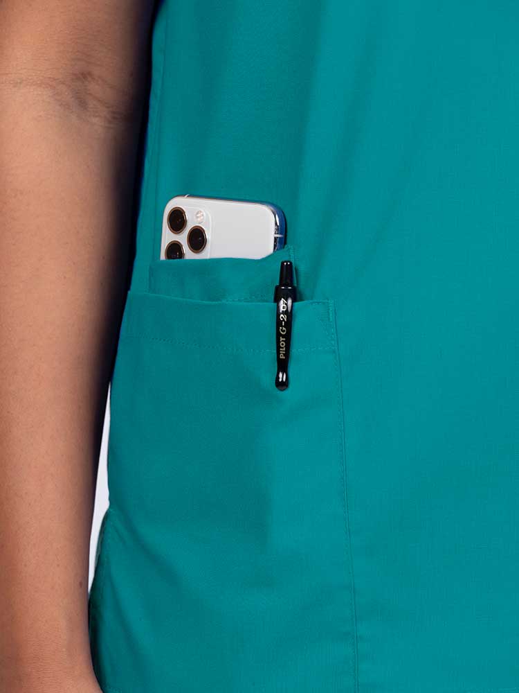 Young female healthcare worker wearing a Luv Scrubs by MedWorks Women's V-neck Scrub Top in teal with a hidden utility pocket/pen slot on wearer's right side.