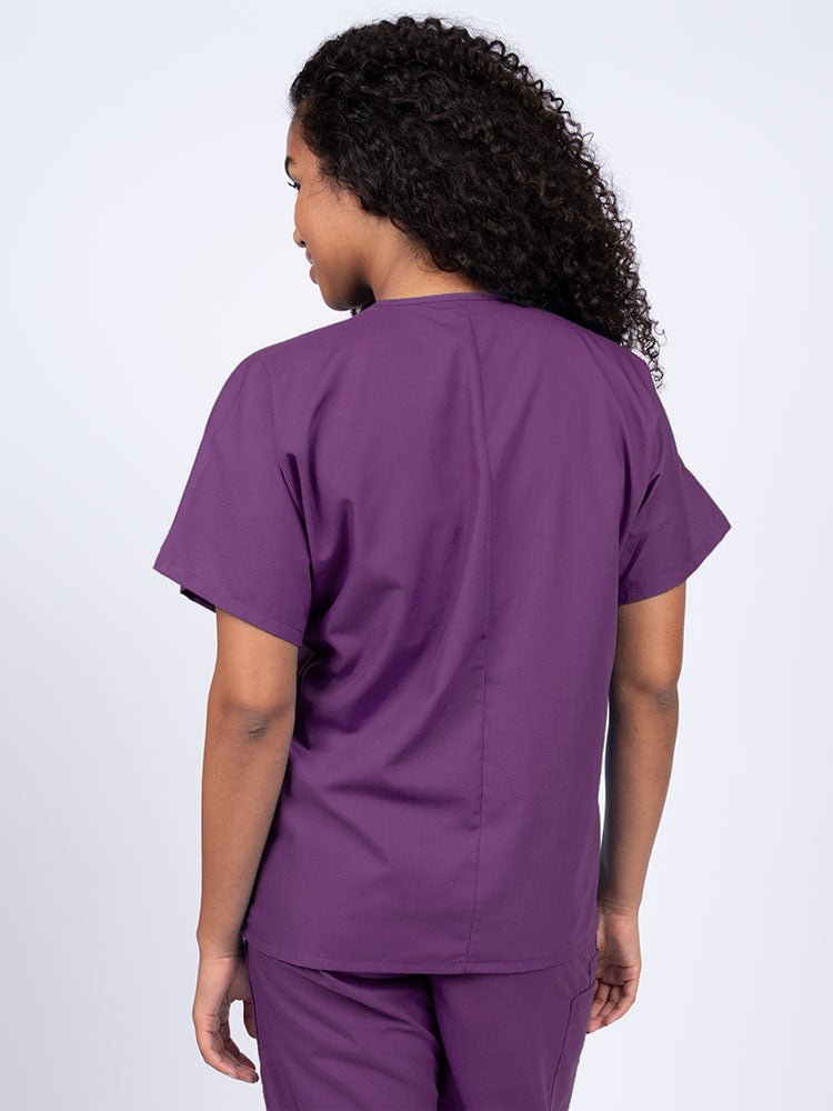 A young female Nurse wearing a Luv Scrubs Unisex Single Pocket V-Neck Scrub Top in Eggplant with a center back length of 27.5".