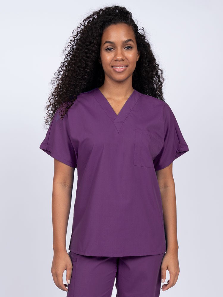 Young female Home Health Aide wearing a Luv Scrubs Unisex Single Pocket Scrub Top in Eggplant featuring a V-neckline.