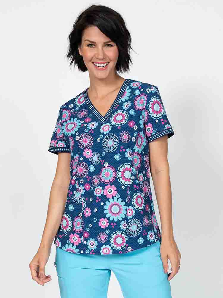 A young female nurse wearing a Meraki Sport Women's Print Scrub Top in "Bloomin Statement" featuring a v-neckline & short sleeves.