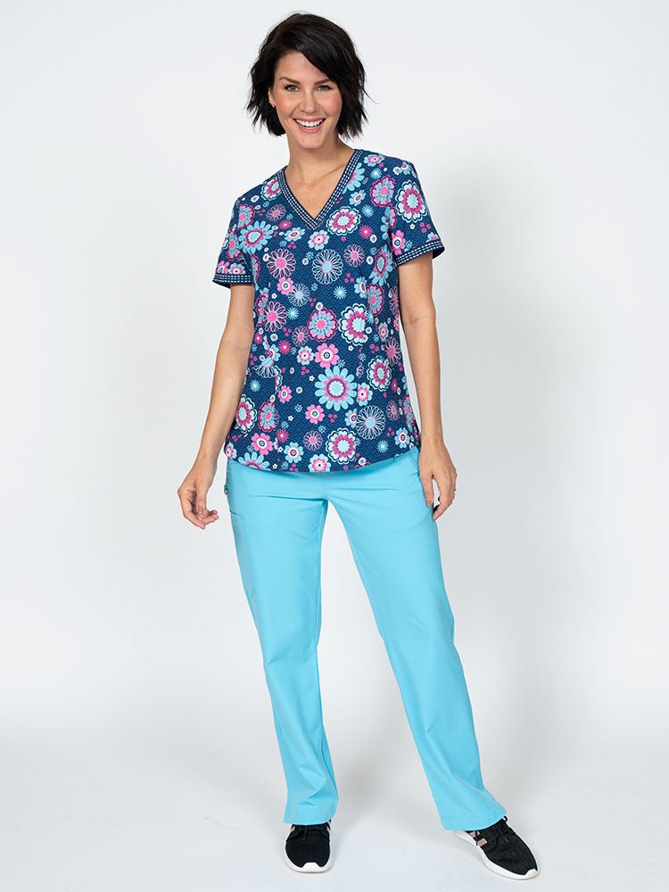 A female LPN wearing a Meraki Sport Women's Print Scrub Top in "Bloomin Statement" featuring 2 front patch pockets for all of your on the job storage needs.