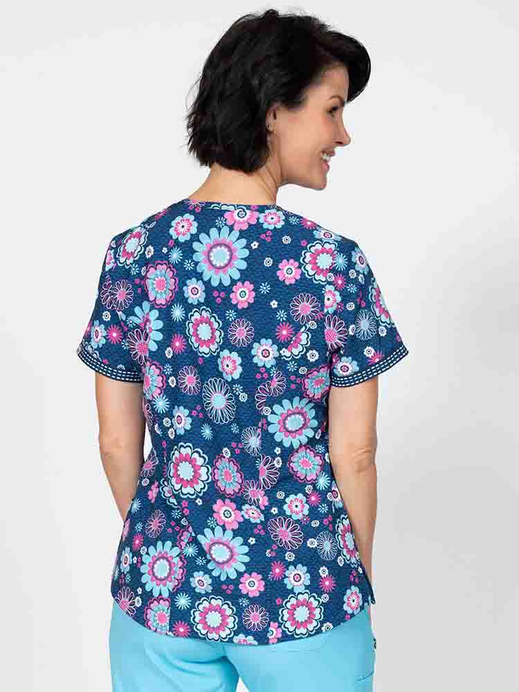 A young female Nurse Practitioner wearing a Women's Print Scrub Top from Meraki Sport in "Bloomin Statement" featuring shoulder yokes & side slits for additional range of motion.