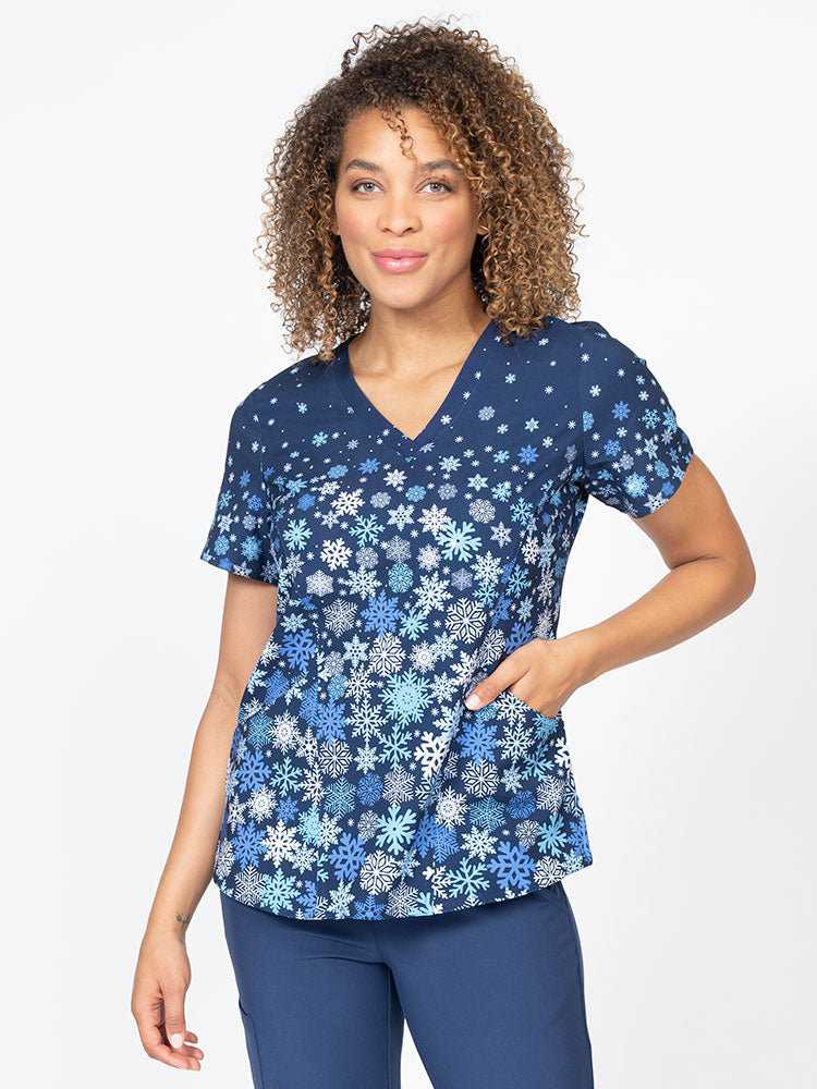 A young female LPN wearing a Meraki Sport Women's Print Scrub Top in "Falling Flakes" featuring a v-neckline & short sleeves.