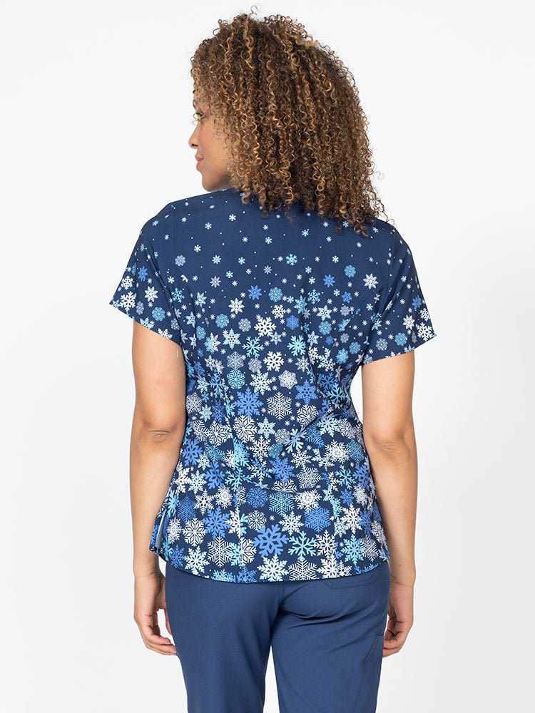 A young female Nurse Practitioner wearing a Women's Print Scrub Top from Meraki Sport in "Falling Flakes" featuring shoulder yokes & side slits for additional range of motion.