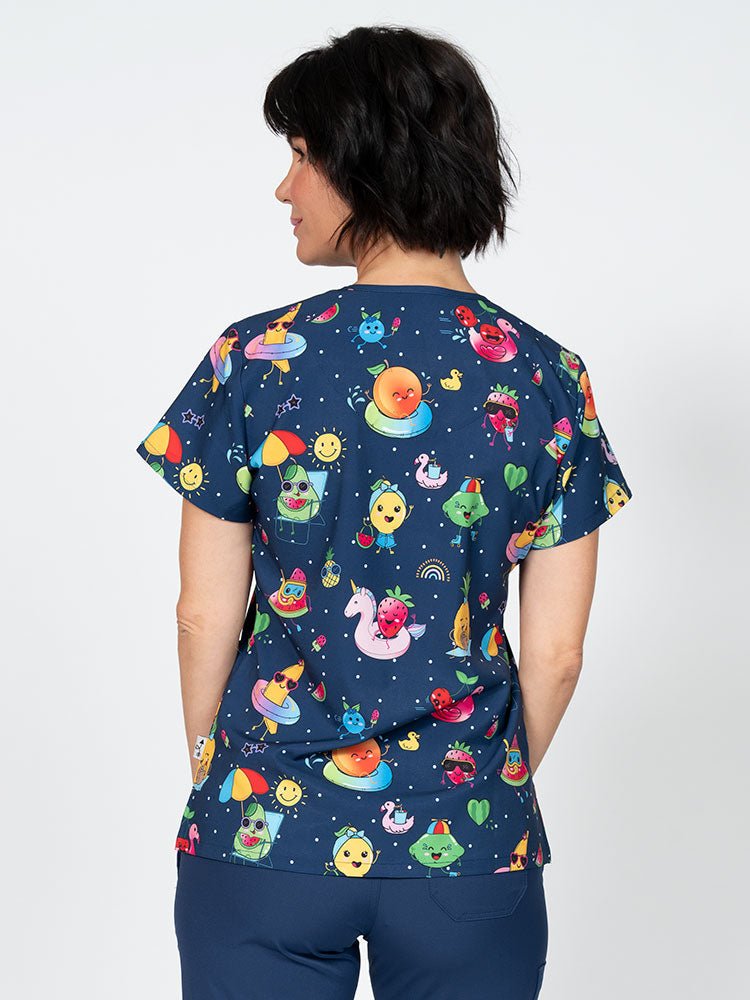 A young lady nurse wearing a Meraki Sport Women's Print Scrub Top in "Fruite-tastic" featuring shoulder yokes & side slits for additional range of motion.