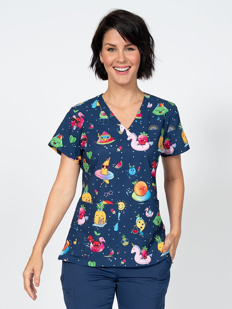 A young female Nurse Practitioner wearing a Meraki Sport Women's Print Scrub Top in "Fruite-tastic" featuring a v-neckline & short sleeves.
