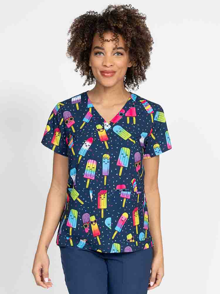 A young female Nurse Practitioner wearing a Meraki Sport Women's Print Scrub Top in "Make Me Melt" featuring a v-neckline & short sleeves.