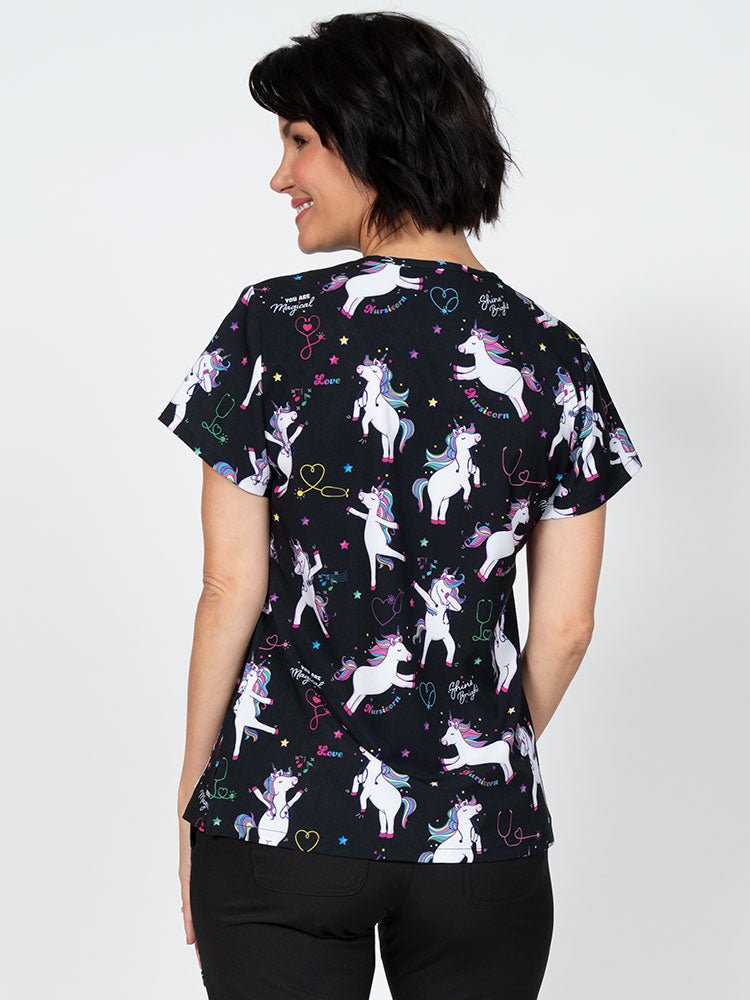 A young lady nurse wearing a Meraki Sport Women's Print Scrub Top in "Nursicorn" featuring shoulder yokes & side slits for additional range of motion.