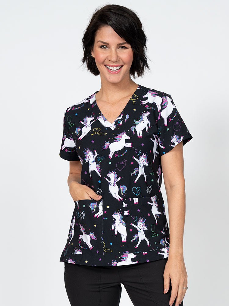 A young female Nurse Practitioner wearing a Meraki Sport Women's Print Scrub Top in "Nursicorn" featuring a v-neckline & short sleeves.