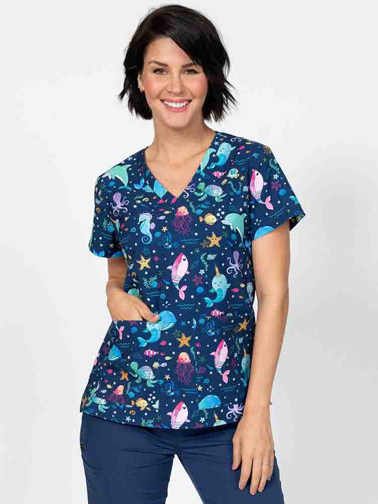 A young female Nurse Practitioner wearing a Meraki Sport Women's Print Scrub Top in "Splish Splash" featuring a v-neckline & short sleeves.