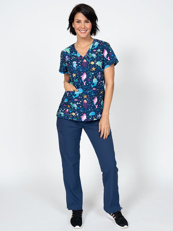 A female LPN wearing a Women's Print Scrub Top from Meraki Sport in "Splish Splash" featuring 2 front patch pockets.