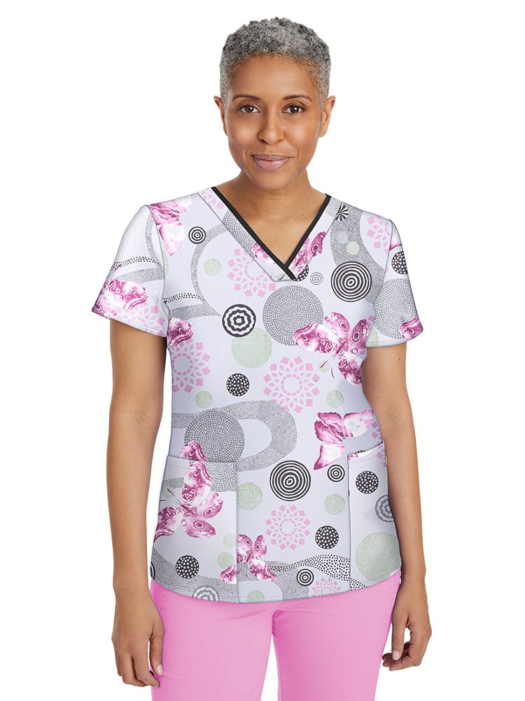 Female nurse wearing a Women's Amanda Print Top from Premiere by Healing Hands in "Delightful Spirit" featuring 2 front welted pockets & an additional interior pocket.