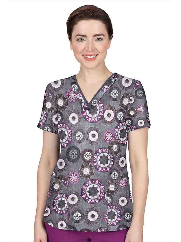 A young female Pediatric Nurse wearing a Premiere by Healing Hands Women's Amanda Print Top in "Festival Carnival" featuring contrast binding and short sleeves.