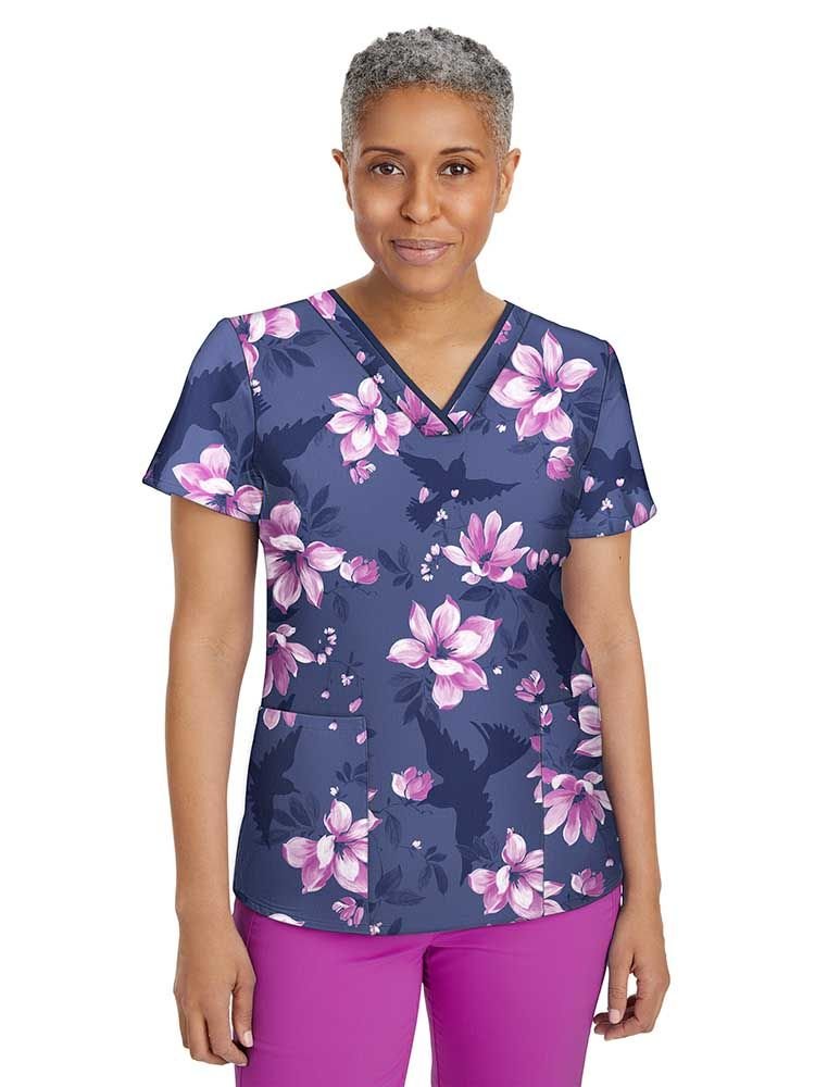A middle aged female Pediatric Nurse wearing a Women's Amanda Printed Scrub Top from Premiere by Healing Hands featuring two front patch pockets and short sleeves.