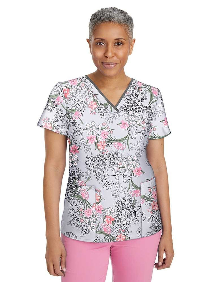 A middle aged female Psychiatric Nurse wearing a Women's Amanda Printed Scrub Top in "Wild Flower" featuring a v-neckline, short sleeves, and a two front patch pockets.