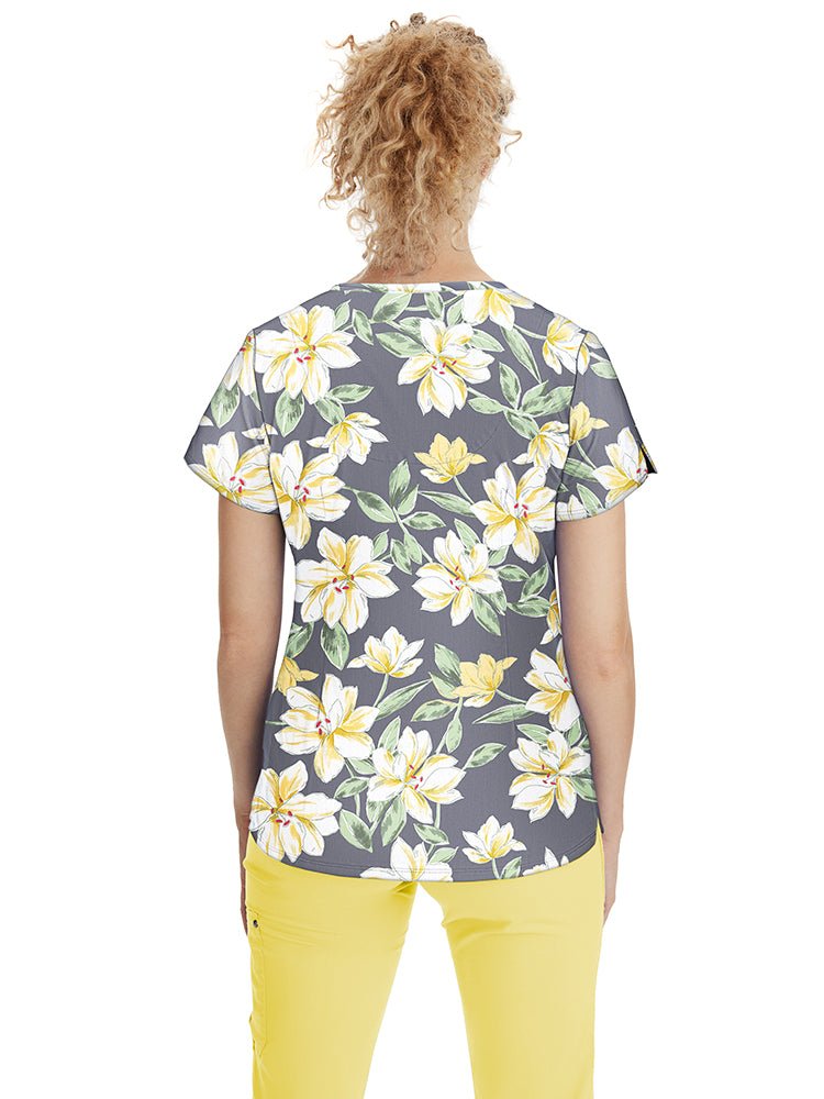 Young nurse wearing a Premiere by Healing Hands Women's Isabel Print Top in "Sunny Azalea" featuring 2 angled front pockets & side slits at the sleeves.