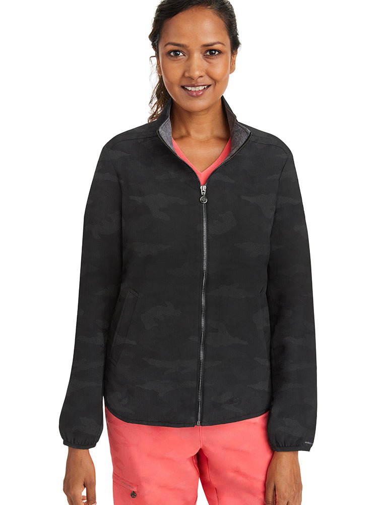 A young female Radiologic Technologist wearing a Purple Label Women's Destini Camo Scrub Jacket in Black size Medium.