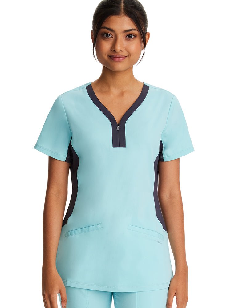 Young female healthcare professional wearing a Purple Label Women's Jessi Y-Neck Scrub Top in "Seabrook" featuring zip-up binding & short sleeves. 