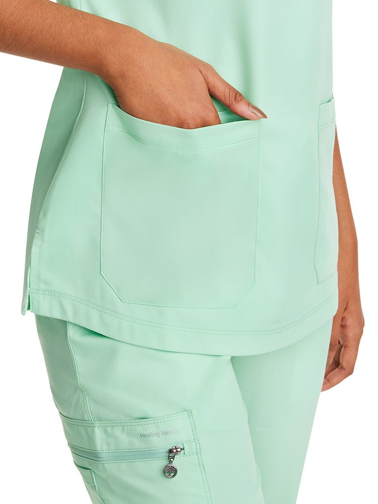 Young female healthcare professional wearing a Purple Label Women's Jill V-Neck Scrub Top in Cool Mint with 2 front patch pockets.