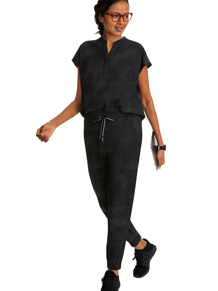 A female Nurse wearing a Purple Label Women's Journey Camo Scrub Top in Black size XL featuring t front welt pockets.